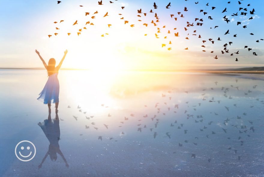 Person with arms raised on a beach as birds fly overhead