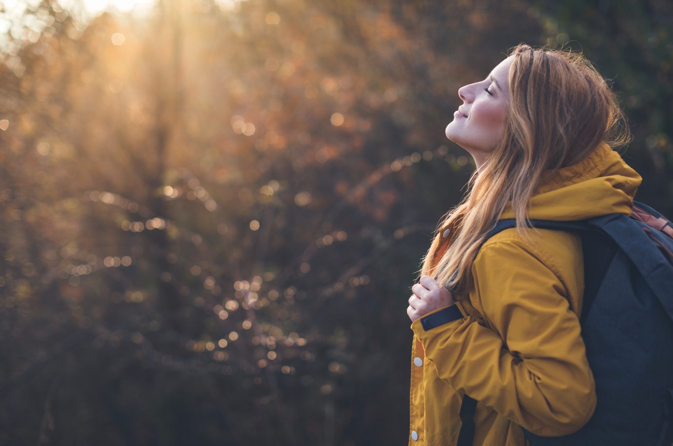Woman in a yellow jacket looking up into the sunlight