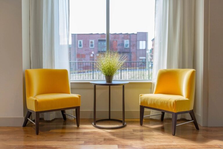 Two yellow armchairs facing each other beside a small table with a plant, in front of a sunny window