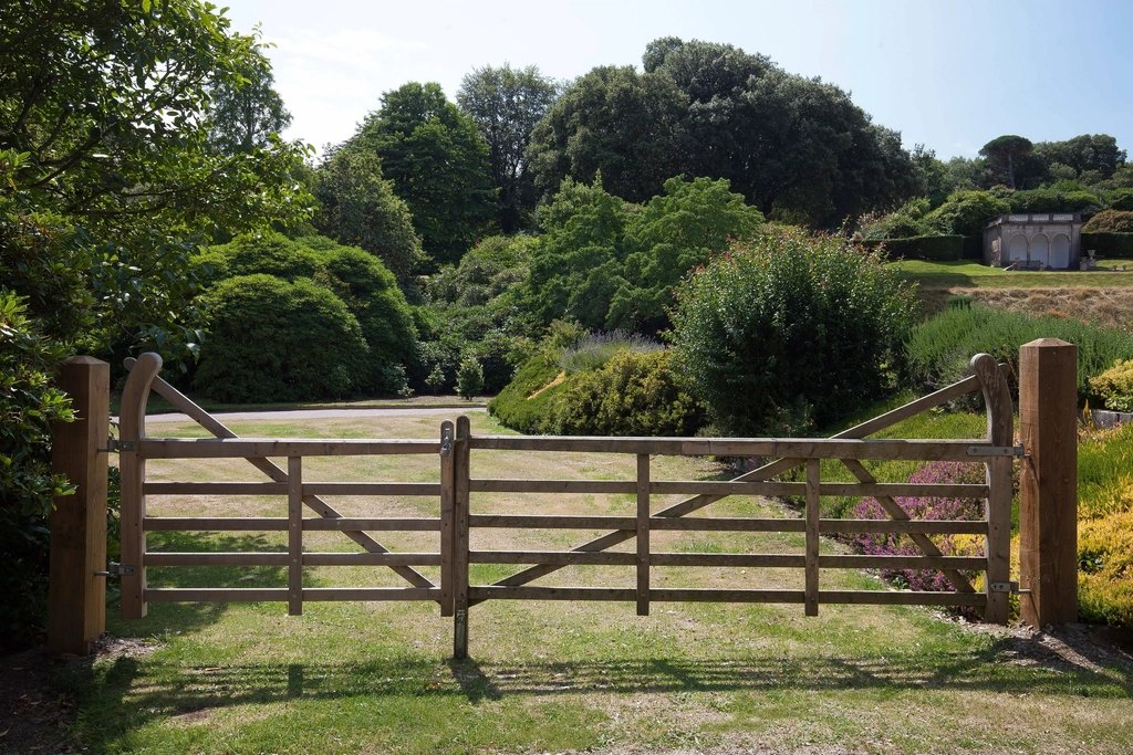 A closed wooden gate between fence posts, with green lawn and trees beyond
