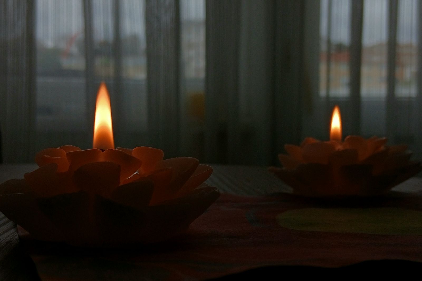 Two candles glow softly in a dim room by a curtained window; grief, remembrance, quiet